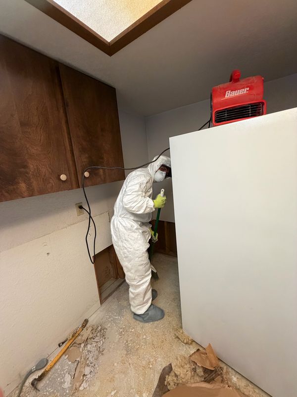 Crew member in a protective suit and respirator sweeping up during a tear-out