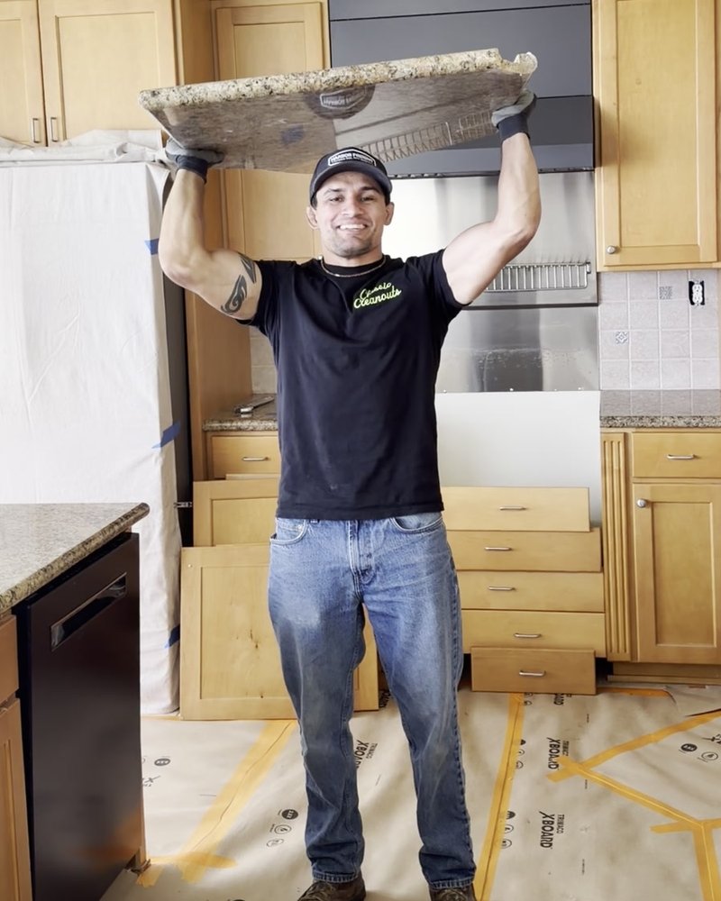 Jason of Classic Cleanouts lifting a granite countertop slab overhead during a kitchen tear-out
